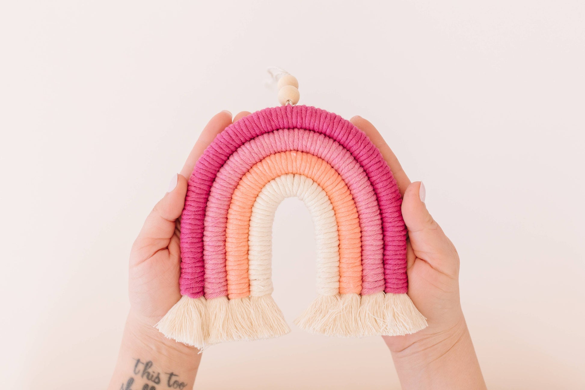 Person holding pink rainbow macrame hanger