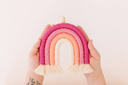 Person holding pink rainbow macrame hanger