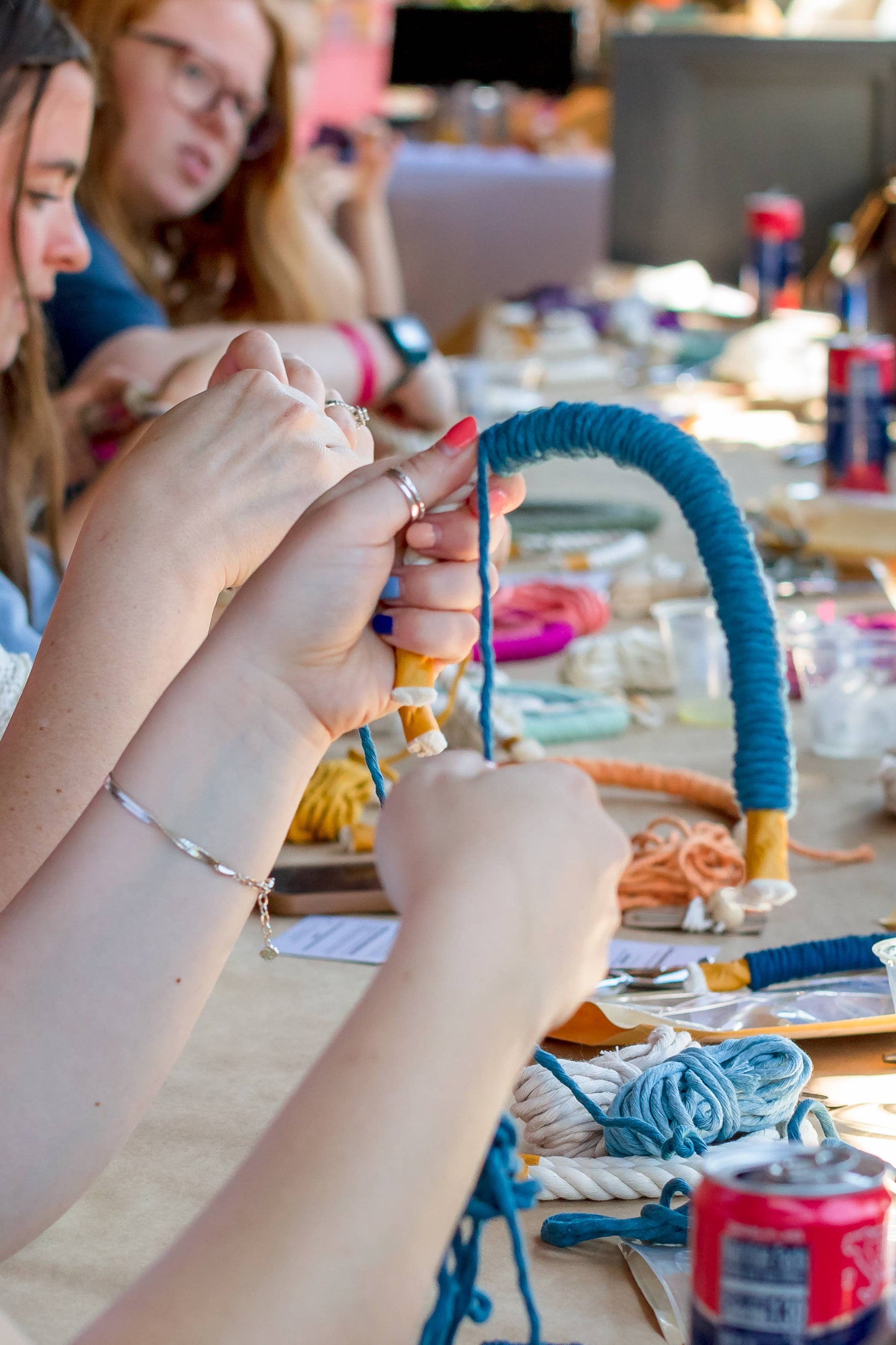 Person crafting with blue yarn at a table with various materials
