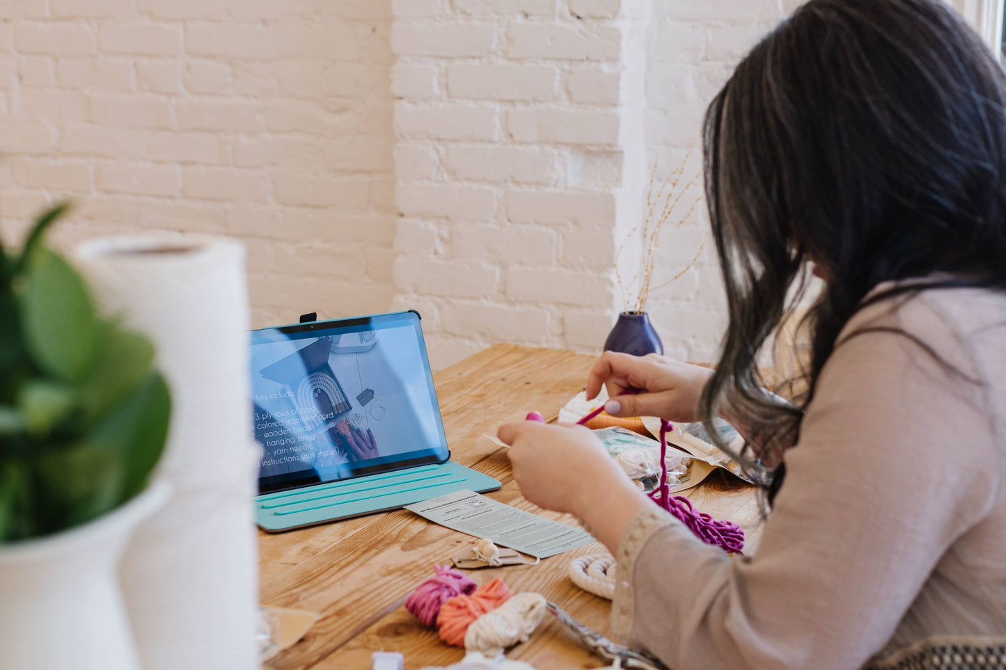 Person holding macrame cord while watching instructions for DIY rainbow kit on tablet.