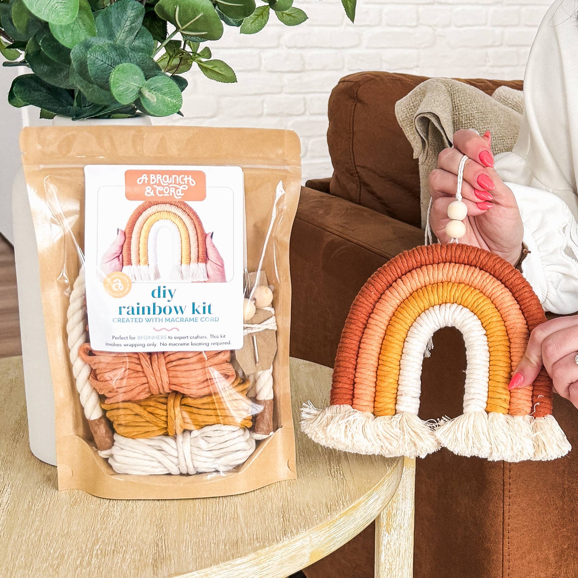 Person holding macrame rainbow kit next to table with kit.