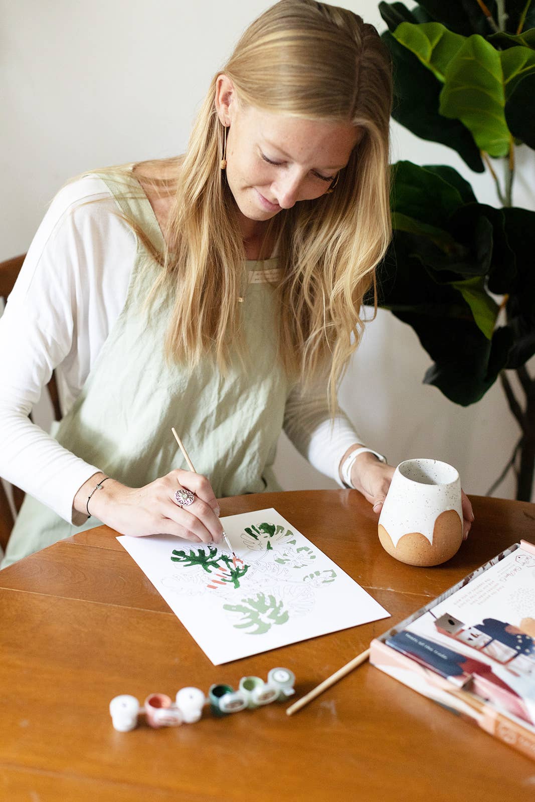 Woman painting a design on paper with a brush at a wooden table.